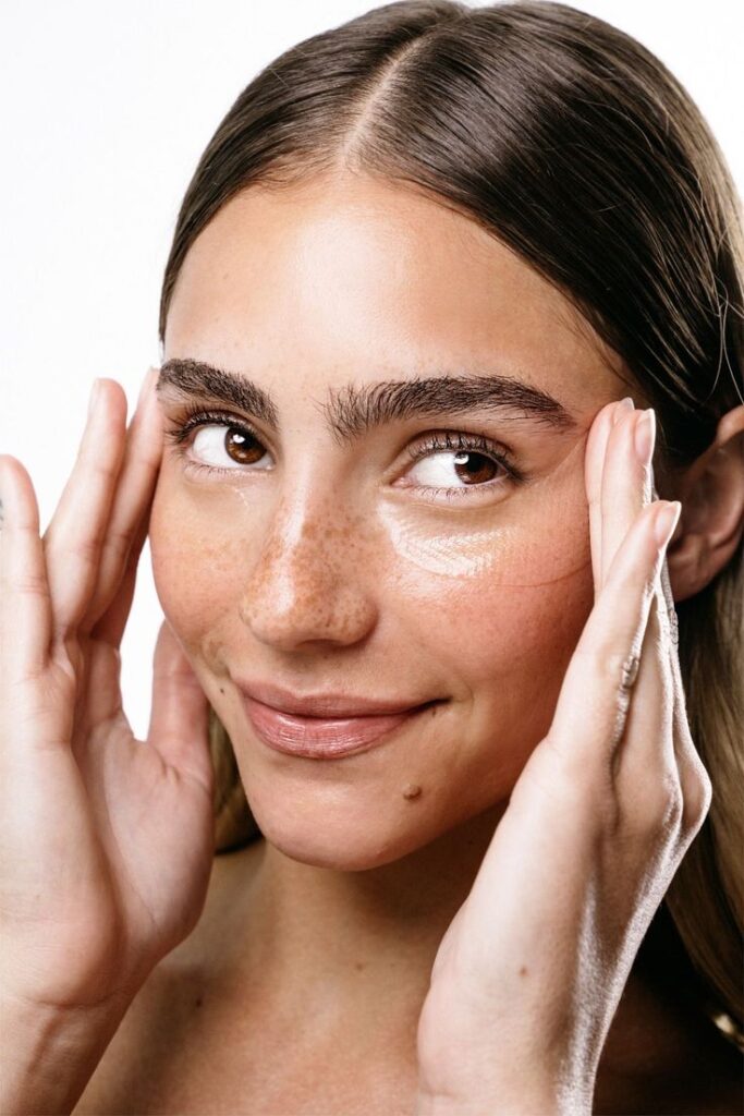 Mujer con pecas aplicando crema bajo los ojos